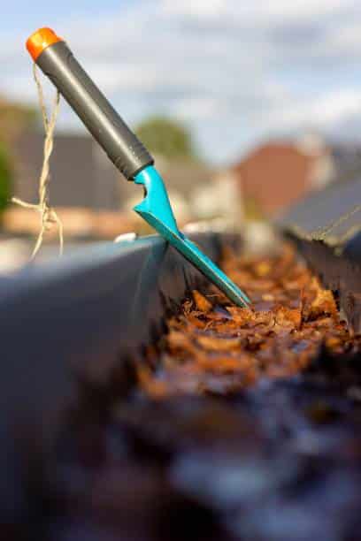 A portrait of a flower or garden shovel standing in a clogged roof gutter. It is used for the annual chore of removing the fallen autumn leaves from the gutter during or after fall.