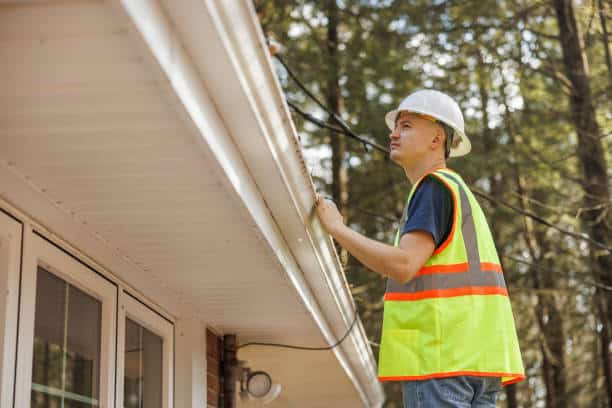 Worker is inspecting the roof of the house to clean the gutter - Denver Gutter Cleaning