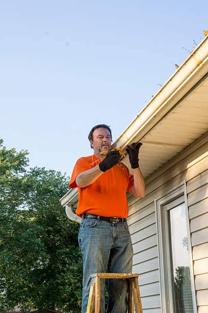 homeowner-cleaning-dry-leaves-from-his-gutters-on-his-home