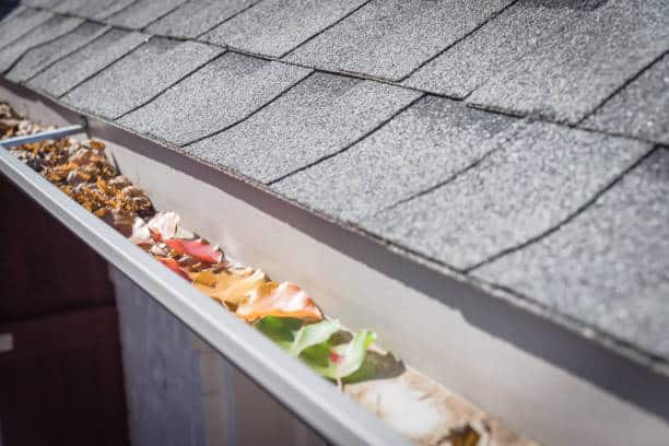 Collection of colorful fall foliage of green, yellow, orange, red, dried brown leaves clogged on metal gutter of residential house near Dallas, Texas, USA. Bradford pear leaf crowded on drainage - Denver Gutter Cleaning